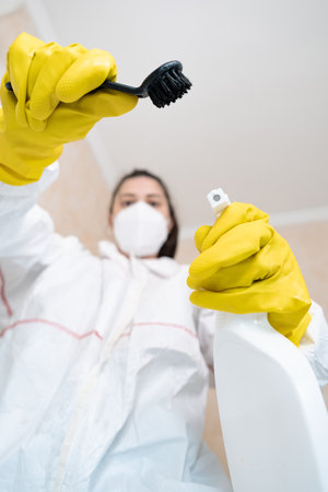 Woman in protective suit and gloves uses chemical cleaning agents, showcasing protective gear for...