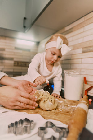 Close-up of a woman's hands rolling dough for sweet gingerbread cookies, with her young daughter helping to prepare Christmas treats.の写真素材