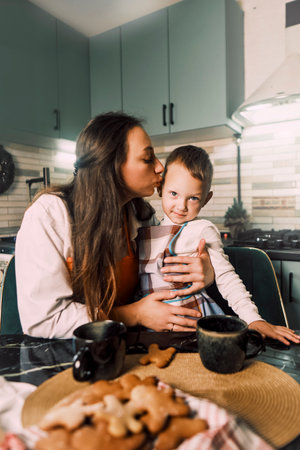 A mother kisses and hugs her son in the kitchen during a festive Christmas dinner, enjoying homemade cookies and tea together.の写真素材