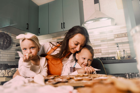 A female pastry chef decorates cookies with frosting, preparing and embellishing treats with children in the kitchen.の写真素材