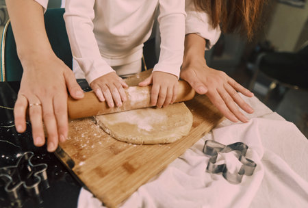 Close-up of a woman's hands rolling dough for sweet gingerbread cookies, with her young daughter...