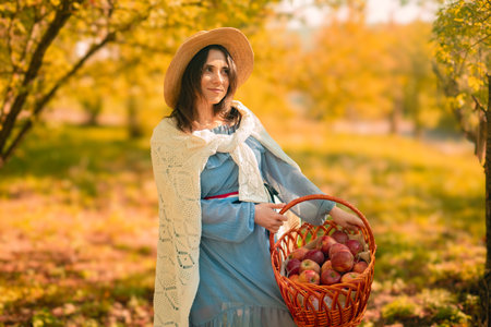 A young woman in a hat holds a basket of apples, showcasing her homegrown harvest for sale at local farmers' markets.の写真素材