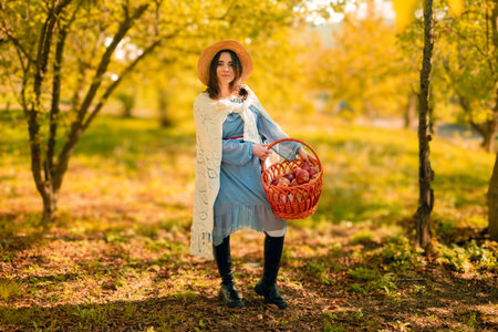 A young woman in a hat holds a basket of apples, showcasing her homegrown harvest for sale at local farmers' markets.の写真素材