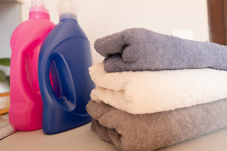 Clean laundry folded on a washing machine, smelling of fresh wash, with detergent and fabric softener in the background.の写真素材