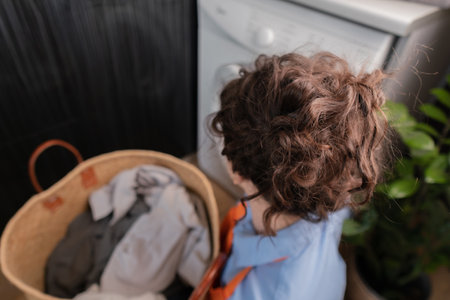 Woman in orange apron turns on washing machine.の写真素材