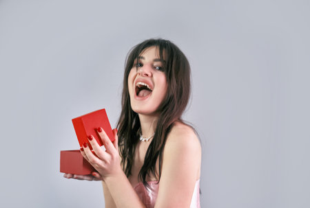 A delighted girl opens a gift box, joyfully looking at her present for Valentine's Day celebration.
