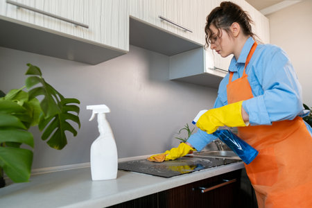 Young woman in an apron cleaning the kitchen, Eco-cleaning: using natural and eco-friendly products that are safe for health and the environment.の写真素材