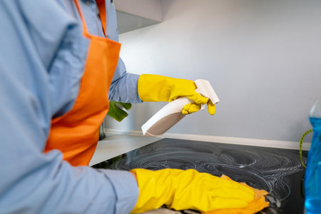 A woman in an apron cleaning the kitchen stove with cleaning products. Wet cleaning with disinfectants kills bacteria left after cooking.の写真素材