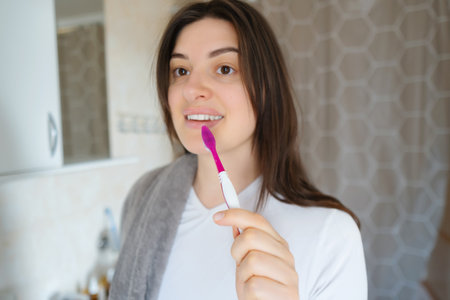 Young woman cares for her dental hygiene in front of the mirror. Starting the day with a smile, brushing for fresh breath.の写真素材