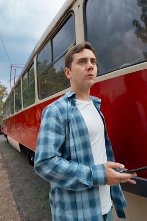 Solo traveler with a phone in hand stands at the stop, waiting for the approaching tram.の写真素材