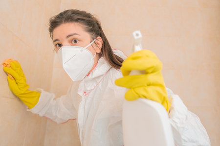 A woman in protective gear cleans bathroom tiles from mold. Cleaning expert disinfects bathroom from mold in a suit and mask.の写真素材