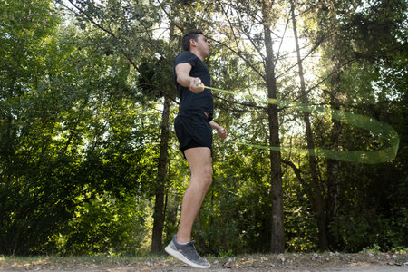 A man actively trains with a jump rope in a green park, boosting energy and strengthening his health.の写真素材
