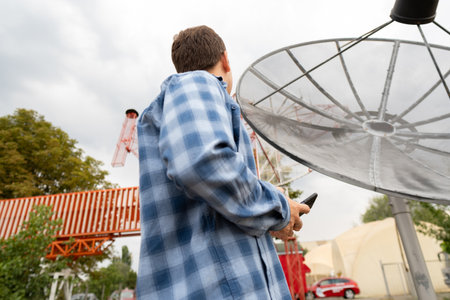 An engineer repairing electronic satellite dishes and radio networks diagnoses issues using a smartphone for troubleshooting.の写真素材