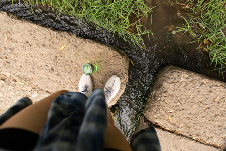 A woman hikes through the forest with a water bottle in hand, turning to cross a river, staying hydrated on her adventure.の写真素材