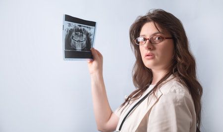 Female dentist carefully examines patient's X-ray to determine the need for treatment.