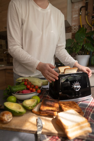 Woman prepares morning avocado toast with vegetables easy and tasty breakfast at home for a healthy...