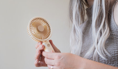 Happy young woman cooling off with her personal fan outdoors on a bright warm sunny day in summer.の写真素材
