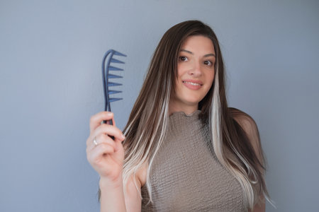 Beautiful hair extensions woman using comb for gentle and comfortable hair care in professional beauty salonの写真素材