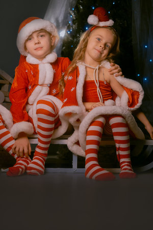 Christmas family moment with children in Santa costumes hugging on a sled by a brightly lit Christmas tree.の写真素材