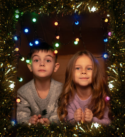 Children in colorful sweaters laughing and playing by Christmas lights enjoying joy and warmth of holiday seasonの写真素材