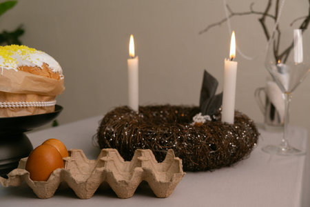 Festive Easter table with cake in white icing, painted eggs in tray, candles, and decorative twig...