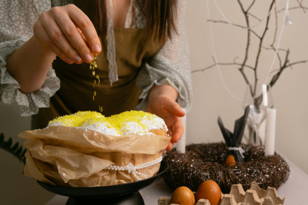 In final moments before Easter, woman carefully sprinkles coconut on Easter cake, creating a festive...