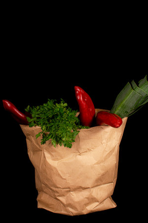 Paper grocery bag with fresh vegetables. Leek, red bell pepper, parsley lie in a paper bag on a black background.の写真素材