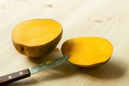 Two halves sliced exotic fruit mango with knife on the wooden table board.