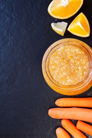 Top view flat lay whole carrots and cut orange, with jar of homemade marmalade jam black table bacground with copy space.の写真素材