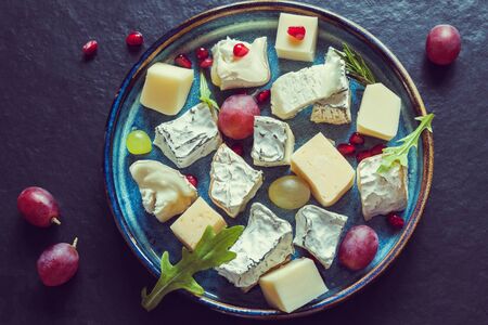 Top view cheese plate assortment of various types of cheese and grapes with pomegranate seeds dark backgroundの写真素材