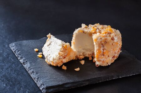 Fresh crotten farm goat cheese and wedge with pieces of mango, hazelnut and pineapple on dark black...