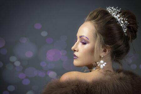 Beautiful model in profile with fashionable makeup in furs. Luxury winter girl on a gray background with bokeh.の写真素材