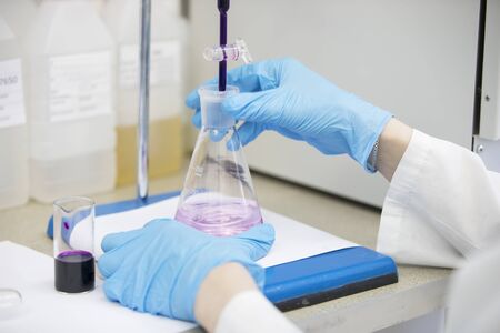 The hands of a technician in blue rubber gloves are holding a flask. Pharmaceutical industry. Chemical laboratoryの写真素材