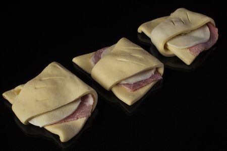 Semi-finished puff pastry with sausage and cheese on a black background