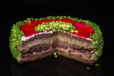 Piece Bright colorful cake with green sprinkling and red jelly on a dark background