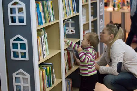 Belarus, the city of Gomel, November 2, 2017. Opening of the children's library department.Grandmother with a baby in her arms near the bookshelves. Earlier development of the baby. Learn to read babiesのeditorial素材