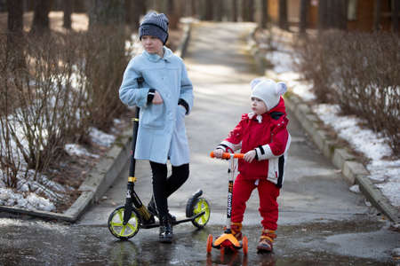 Belarus, the city of Gomel, March 09, 2019. Celebration Maslenitsa.Children with scooters. The older sister and younger brother are playing on the street.のeditorial素材
