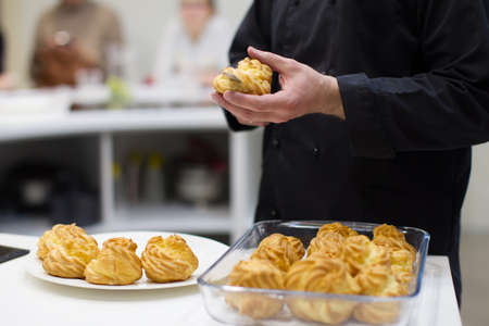 The cook prepares eclairs. Cut the eclairs and lay the cream