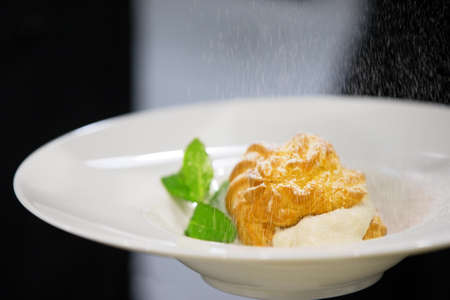 Eclair on a plate with mint leaves sprinkled with powdered sugar
