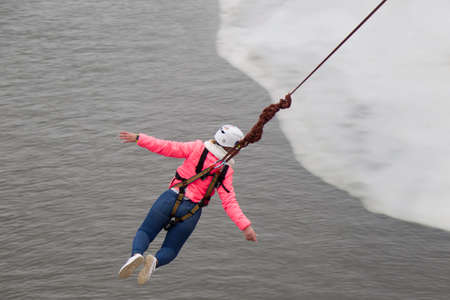 Belarus, Gomel, March 08, 2019. Jumping from the bridge to the rope.Ropejumping.Dangerous hobbies.Brave woman jumping from the bridge against the skyの写真素材