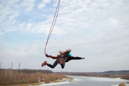 Belarus, Gomel, March 08, 2019. Jumping from the bridge to the rope.Ropejumping.Dangerous hobbies.Brave woman jumping from the bridge against the skyのeditorial素材