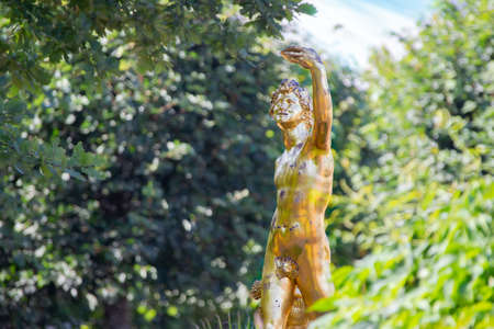 Russia, Peterhof, July 27, 2019. Palace territory of Peter the Great.Golden statue of a naked man on a background of foliageのeditorial素材