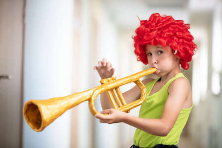 A child in a bright wig plays the trumpet. Funny boy with a toy musical instrument. Future artist