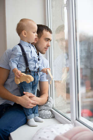 Father and little son are looking out the window. A man is playing with a childの写真素材