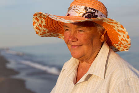 Beautiful elderly woman in a hat on the background of the sea. Face of an old woman with a smile. Grandma on vacationの写真素材