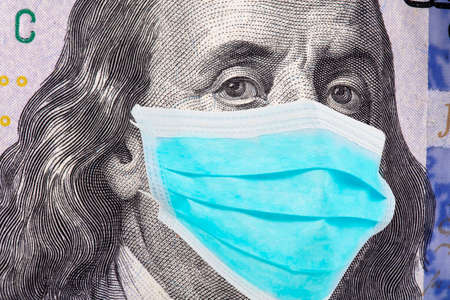 Benjamin Franklin in a mask on a 100 dollar bill isolated on white background. Concept of prevention of money from crisis.の写真素材