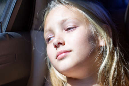 The face of the child in the car. Beautiful teenager girl lit by the sun in transport. Tired passenger.の写真素材