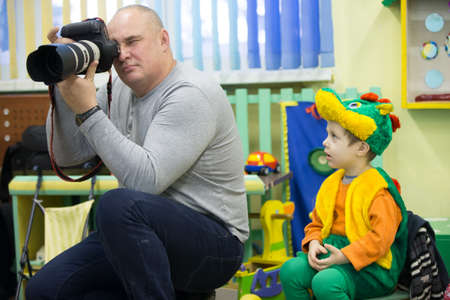 Belarus, the city of Gomil, December 16, 2016. Parent day in kindergarten. Photographer works in kindergarten. A man with a professional camera and a child in a fancy dress.のeditorial素材
