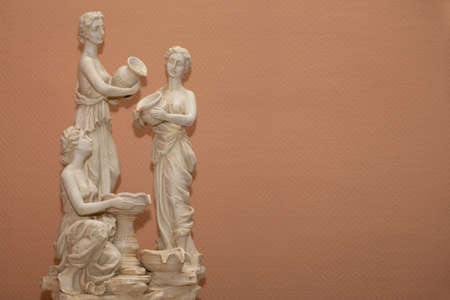 Background statues of three Greek women on a beige background.