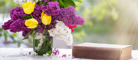 Spring background. Lilac and tulips in a glass jar on the table, also an old book. Beautiful flowers...